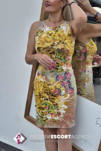 Woman in floral dress admires reflection in mirror.